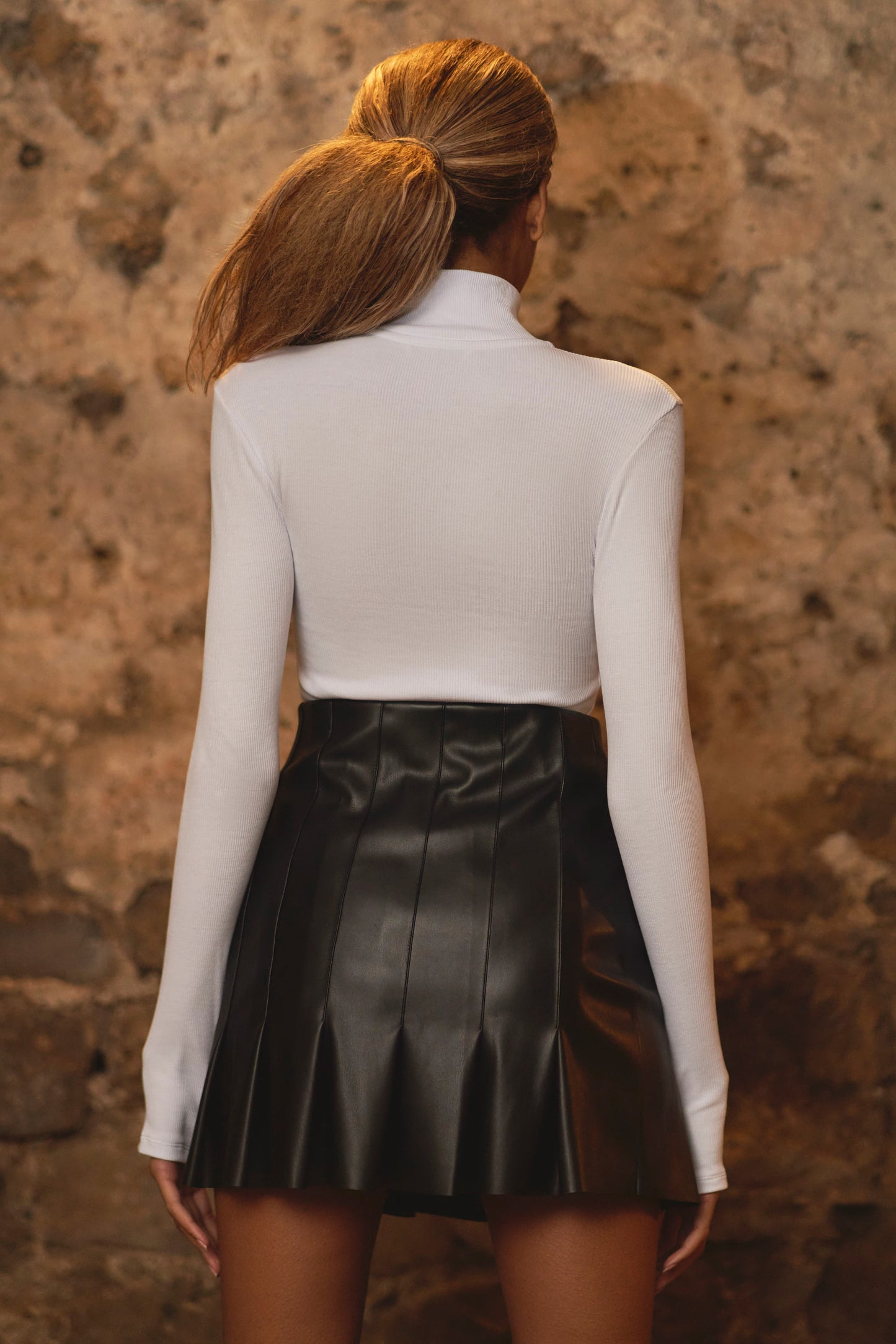 back view of model wearing luxury leather pleated skirt and white bodysuit