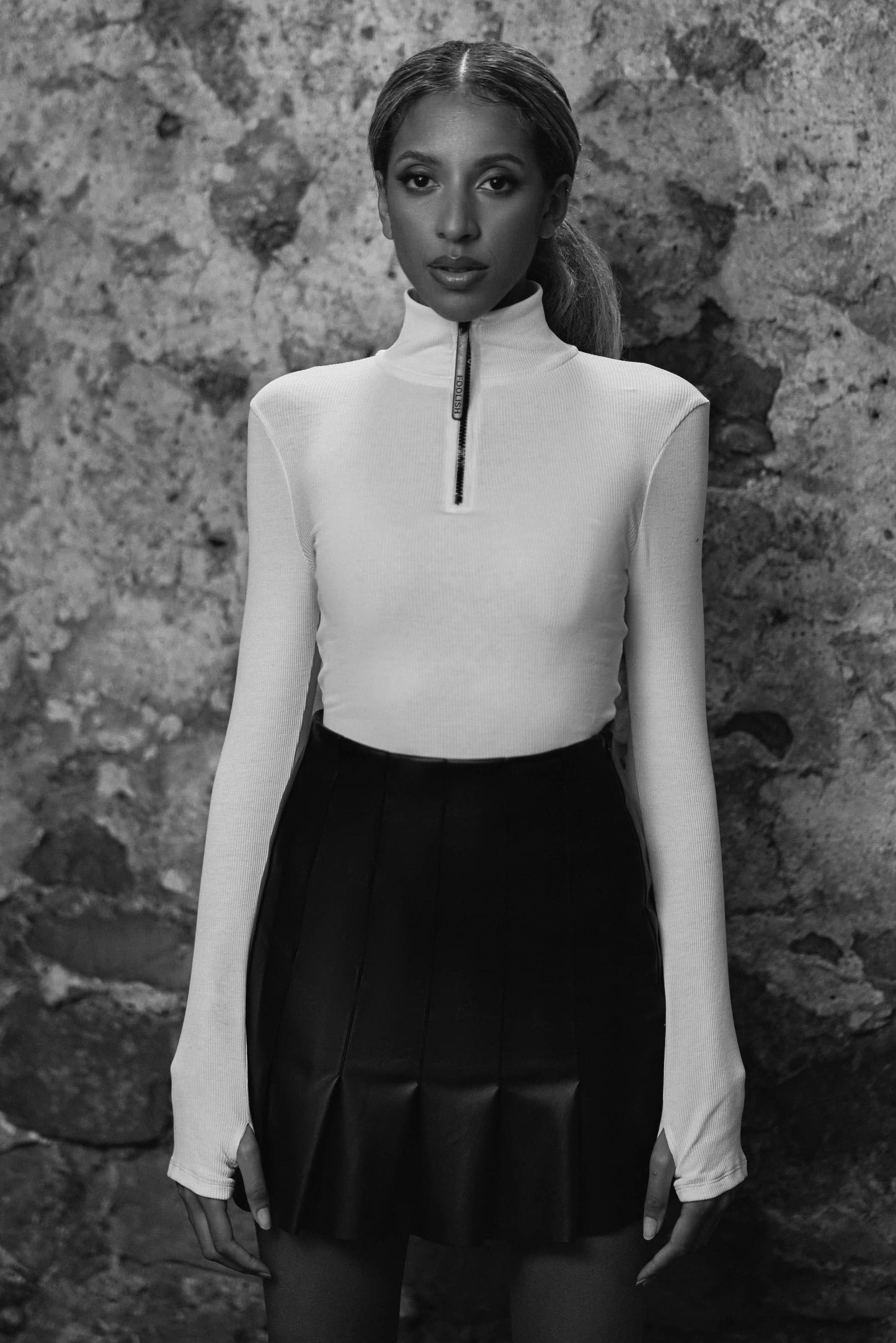model styled in womens black leather pleated skirt with long sleeve white bodysuit