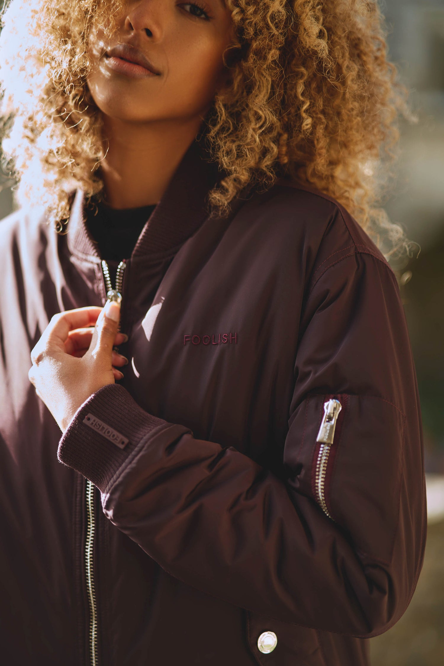 close up of branding details on womens contemporary bomber jacket in burgundy