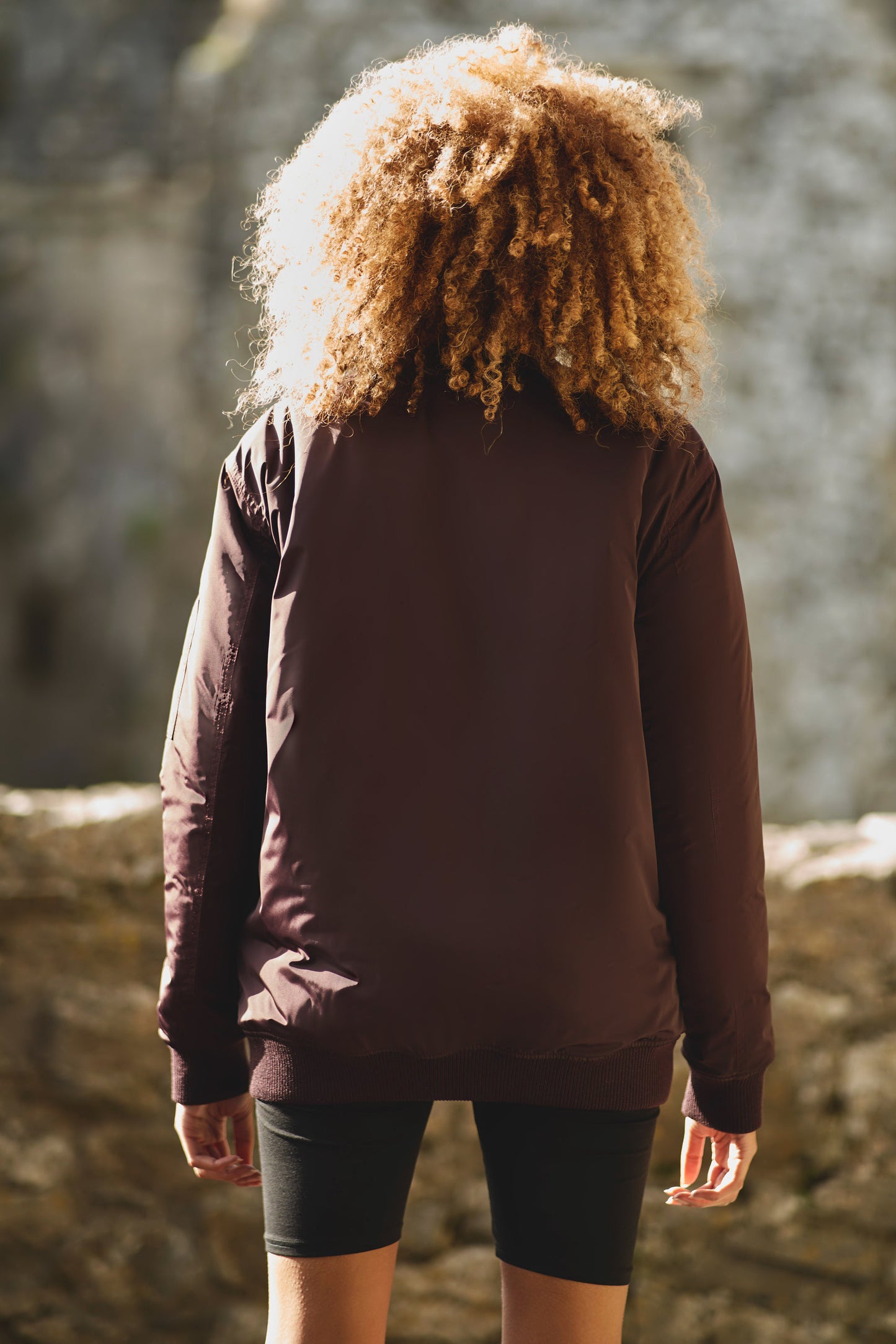 back view of womens bomber jacket in burgundy styled with black shorts