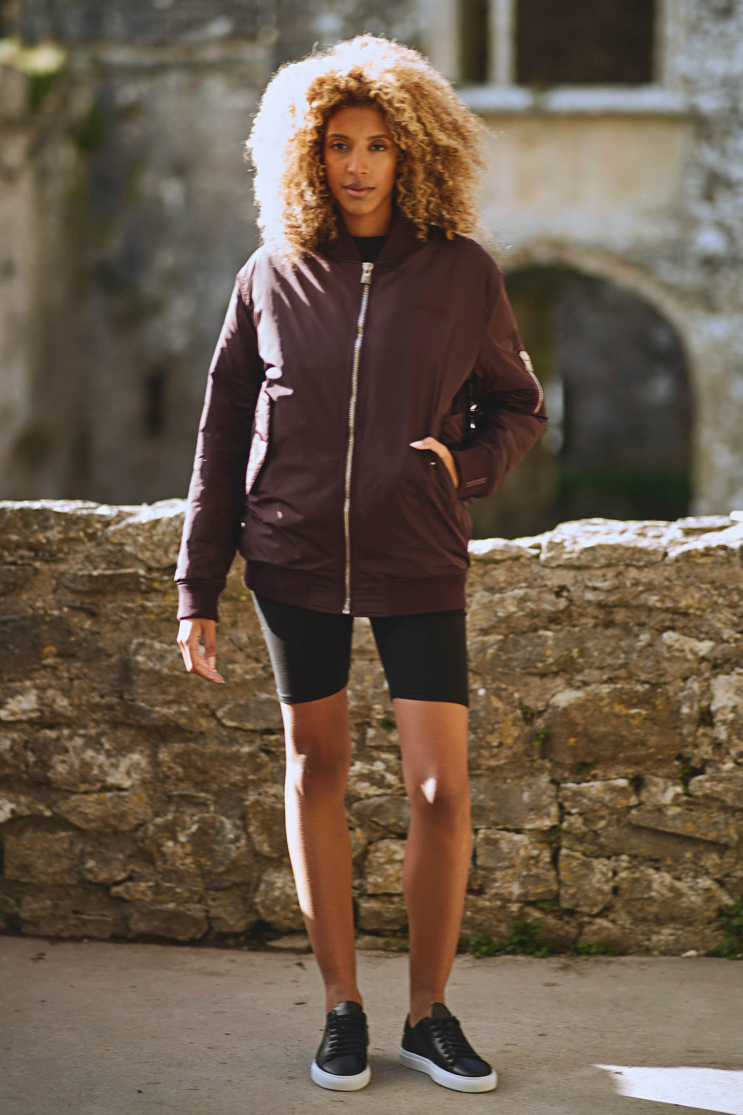 model with one hand in pocket of contemporary womens bomber jacket in burgundy